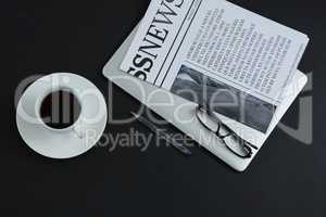 Black coffee, spectacles, pen, laptop and newspaper on black background