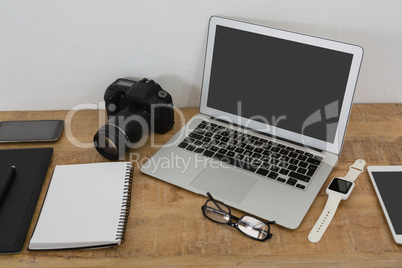 Laptop, wristwatch, notepad, camera and mobile phone on wooden table