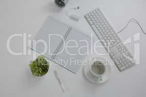 Keyboard, pot plant, pen, book, coffee cup and saucer on table