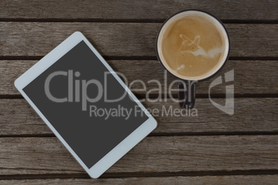 Digital tablet and cup of coffee on wooden plank