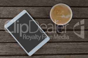 Digital tablet and cup of coffee on wooden plank