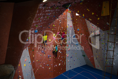 View of trainer and athletes rock climbing in fitness club