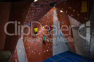 View of trainer and athletes rock climbing in fitness club