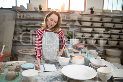 Female potter checking the orders in notebook