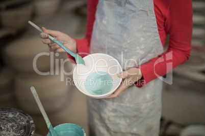Mid section of female potter painting bowl