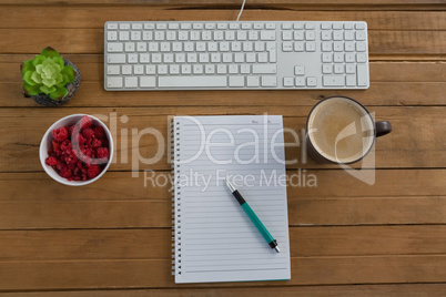 Coffee, keyboard, pot plant, notepad, pen and raspberry on wooden plank