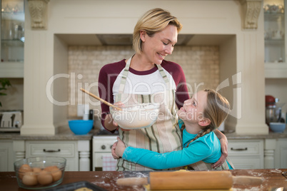 Daughter hugging mother while preparing cookies in kitchen