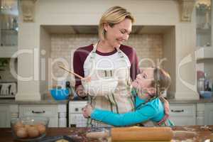 Daughter hugging mother while preparing cookies in kitchen
