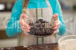 Girl holding bowl of dried blue berries in kitchen