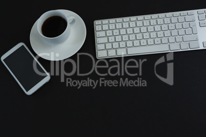 Keyboard, mobile phone and black coffee on black background
