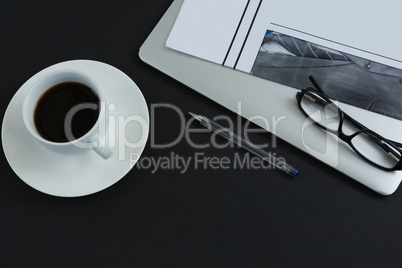 Black coffee, spectacles, pen, laptop and newspaper on black background
