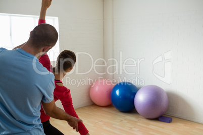 Rear view of instructor assisting student in exercising at yoga studio