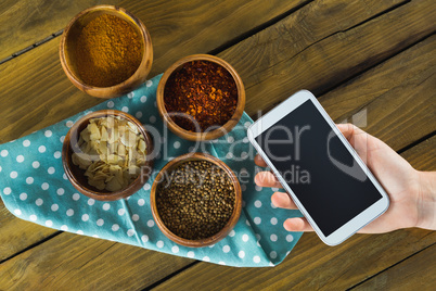 Hand holding mobilephone and various spices in bowlq