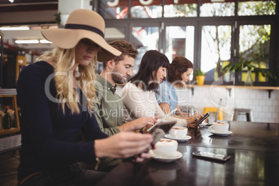 Friends using mobile phones while sitting with coffee cups in cafe