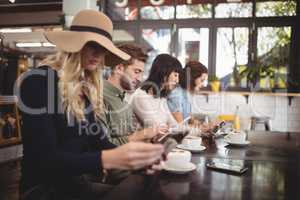 Friends using mobile phones while sitting with coffee cups in cafe