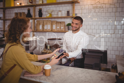Smiling young woman paying through card to waiter at counter