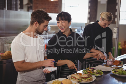 Cheerful chef pointing at food to waiter by female colleague