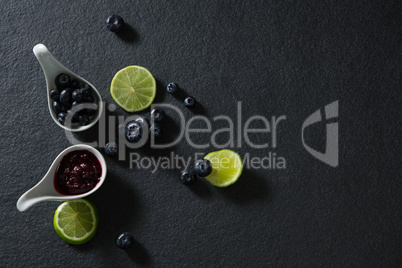 Slice of lemon and spoon with blueberries on black background