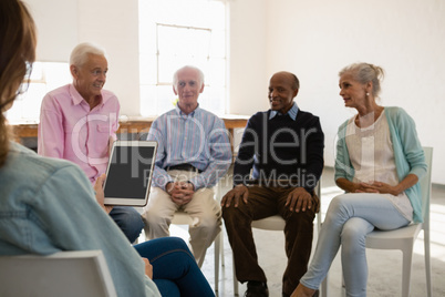 Woman holding tablet computer while discussing with senior adults