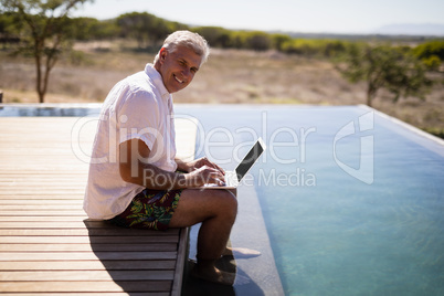 Man using laptop near poolside during safari vacation