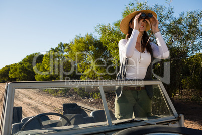 Young woman looking through binoculars standing in off road vehicle