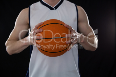 Player holding basketball against black background