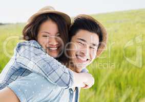 Millennial couple piggy back against blurry meadow