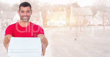 Delivery man holding out pizza box against blurry housing estate with flares