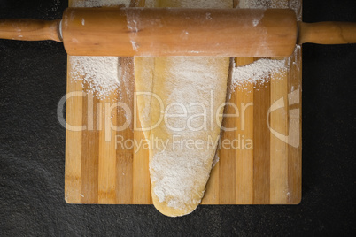 Directly above shot of wooden rolling pin on dough over cutting board