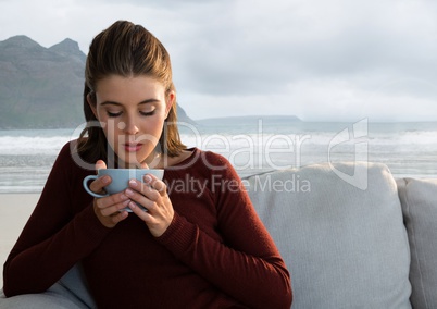 Woman drinking from cup on couch with sea mountain landscape