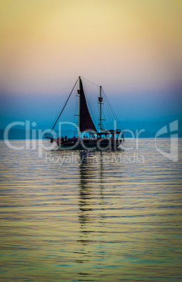 Silhouette of a lonely sailboat on calm lake at sunset, colorful sky.