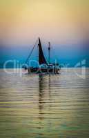 Silhouette of a lonely sailboat on calm lake at sunset, colorful sky.