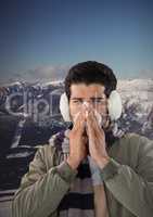 Man blowing nose with earmuffs and snow mountain landscape