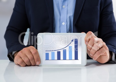 Businessman with tablet at desk and bar chart arrow