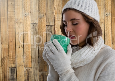 Woman against wood with warm gloves hat and scarf and cup