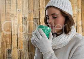 Woman against wood with warm gloves hat and scarf and cup