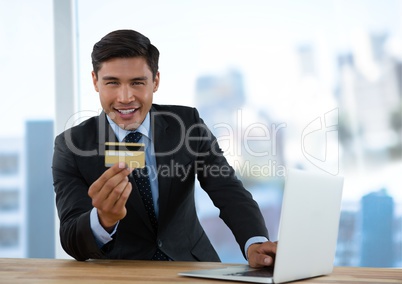 Businessman at desk with laptop with bright background and bank card