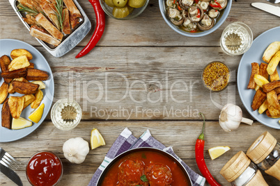 Dining table with a variety of meals and snacks. Meatballs, baked potato wedges, meat, mushrooms, ketchup. Rustic style. Wooden background, top view.