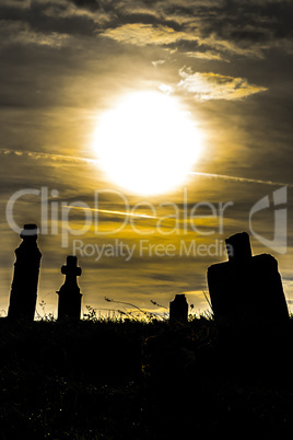 Old cemetery at sunset, silhouette of tombstones, dramatic sky.