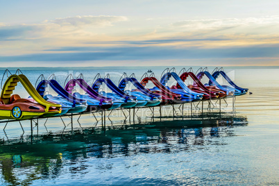 Colorful paddle bikes on calm summer lake.