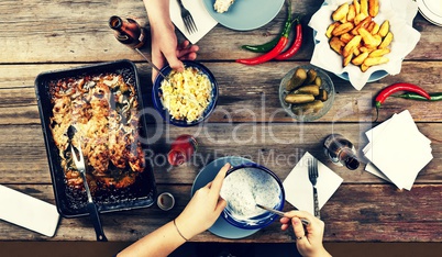 Couple of young people at the dinner table with a variety of foods, baked chicken legs, potatoes barbecue, beer, pickles and snacks,