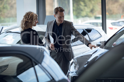 Confident salesman showing car to customer in showroom