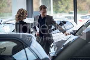Confident salesman showing car to customer in showroom