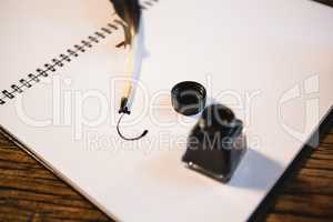 Diary and quill pen with ink bottle on wooden table in living room