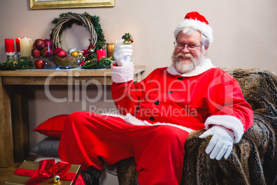 Santa claus holding a gift and sitting on the sofa at home