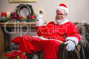 Santa claus holding a gift and sitting on the sofa at home