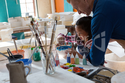 Male potter assisting girl to paint bowl