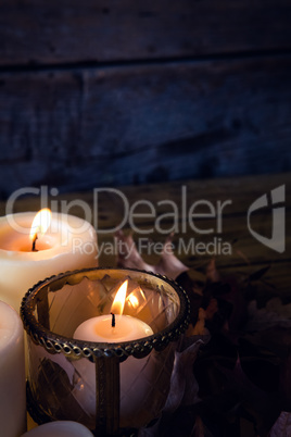 Lit candles and dry leaves on table