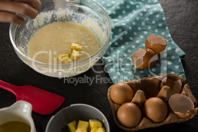 Woman adding butter cubes to batter of beaten eggs and milk in a bowl