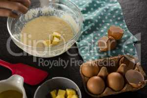 Woman adding butter cubes to batter of beaten eggs and milk in a bowl